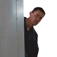 a man in a blue shirt is peeking out from behind a white wall