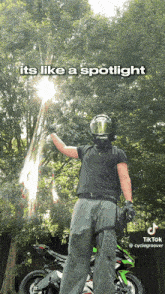 a man in a helmet stands in front of a motorcycle with the sun shining through the trees above him