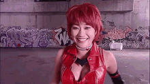 a woman with red hair is smiling in front of a wall with graffiti on it .