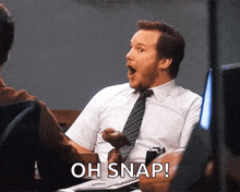 a man in a white shirt and tie is sitting at a table with his mouth open and says oh snap