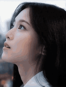 a close up of a woman 's face with a white shirt on looking up .