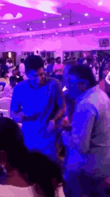 a group of people are dancing in a room with purple lighting
