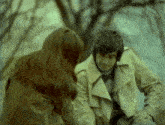 a man in a trench coat is talking to a woman