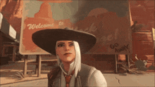 a woman in a cowboy hat is standing in front of a welcome sign
