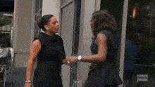 two women in black dresses are standing next to each other and talking .