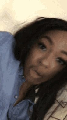 a woman in a blue shirt is making a funny face while laying on a bed .