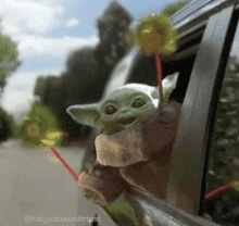 a baby yoda is sticking its head out of the window of a car .