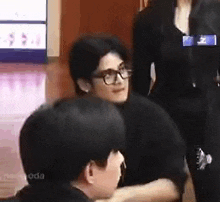 a man wearing glasses is sitting at a table with a woman standing behind him .