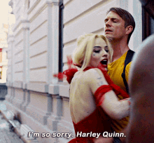 a woman in a red dress says i 'm so sorry harley quinn in front of a man in a yellow shirt