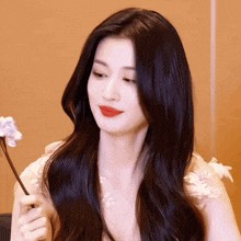 a woman with long black hair holds a flower in her hand