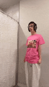 a person wearing headphones and a pink shirt with a picture of a man on it is standing in front of a shower curtain