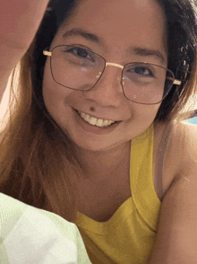 a woman wearing glasses and a yellow shirt smiles for the camera