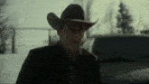 a man in a cowboy hat and suit is standing in front of a car .