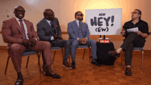 a group of men are sitting in front of a sign that says hey