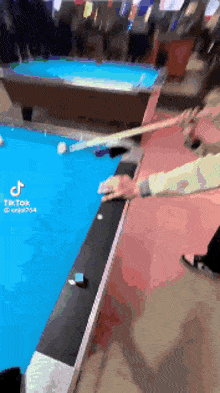 a person is holding a pool cue in front of a pool table with tiktok written on the bottom of the screen .