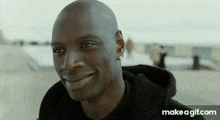 a bald man is smiling and wearing a black hoodie and earrings .