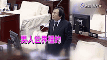 a man in a suit and tie is speaking into a microphone in front of a computer monitor with chinese writing on it