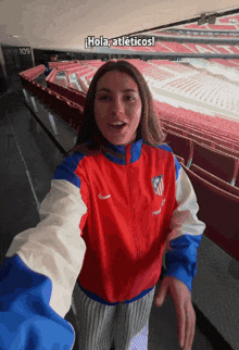 a woman in a red white and blue nike jacket takes a selfie in a stadium