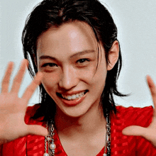 a woman wearing a red shirt and a pearl necklace is smiling and waving