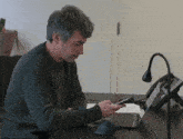 a man sits at a desk with a phone and a laptop looking at his phone