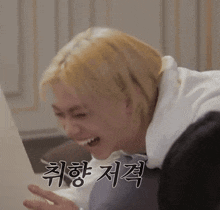 a man with blonde hair is making a funny face while sitting on a bed with a laptop .