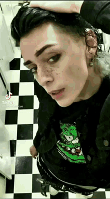 a woman with freckles is standing on a checkered floor in a bathroom .