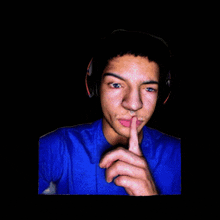 a man wearing headphones and a blue shirt holds his finger to his mouth