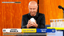a bald man is holding a white ball in front of a microphone and a sign that says viperissimo trash