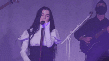 a woman singing into a microphone while a man plays a guitar in the background