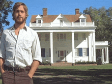 a man in a white shirt stands in front of a large white house
