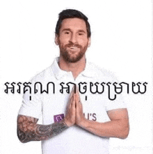 a man with a beard and a tattoo on his arm is wearing a white shirt and praying with his hands together .