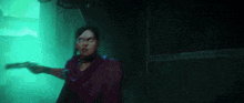 a woman is holding a gun in a dark room with a green light behind her .