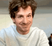 a man with curly hair is smiling for the camera while wearing a white sweater .
