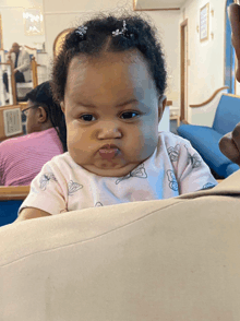 a baby in a pink shirt with butterflies on it looks at the camera