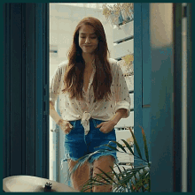 a woman in a white shirt and blue shorts is standing in a doorway with her hands in her pockets