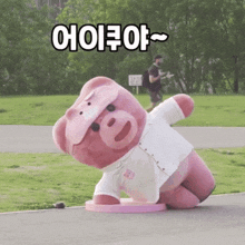 a pink teddy bear wearing a white shirt is kneeling down on the ground