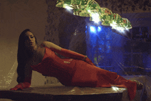 a woman in a red dress is laying on a table under a lamp
