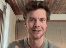 a man in a gray sweater is giving a thumbs up while talking on a video call .