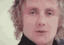 a close up of a man 's face with curly hair and blue eyes looking at the camera .