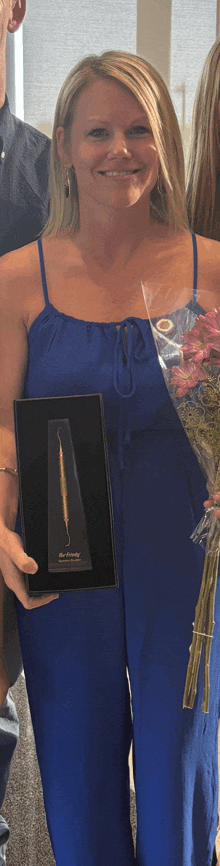 a woman in a blue jumpsuit is holding a trophy and a bouquet of flowers