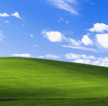 a grassy hill with a blue sky and white clouds
