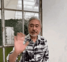 a man with a beard is waving his hand in front of a large window .