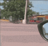 a car 's rear view mirror shows a street with trees and a building .