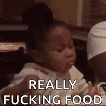 a little girl is sitting at a table eating food and making a face .