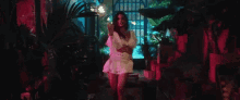 a woman in a white dress is dancing in a dark room with a pink light behind her .