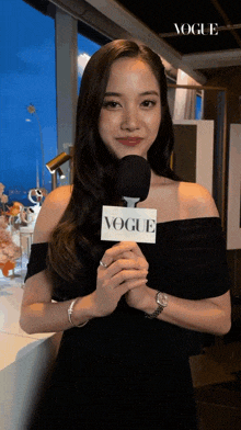 a woman in a black dress is holding a microphone that says vogue on it