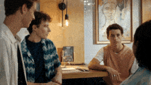 a group of young men are sitting at a table in front of a painting of a woman 's face