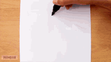 a person drawing on a piece of paper with drawbook written on the bottom right