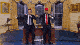 two men in suits and ties are dancing in front of a desk