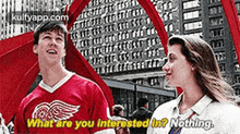 a man and a woman are standing next to each other and the man is wearing a red jersey with the word wings on it .
